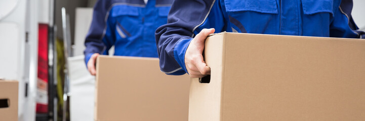 Close-up Of Two Movers Carrying Cardboard Box