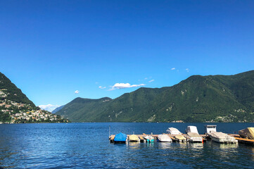 Stunning landscape of picturesque Lake Lugano and the green lush Swiss Alps in the distance. Idyllic town Lugano, Switzerland, on a sunny summer day.