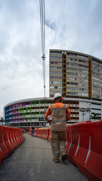 Medellin, Antioquia, Colombia - June 2 2022: Construction Worker Walks On The Road In Direction Of A Shopping Center Between Orange Plastic Barriers Seen From Behind