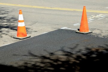 Construction cones marking part of road with a layer of fresh asphalt.