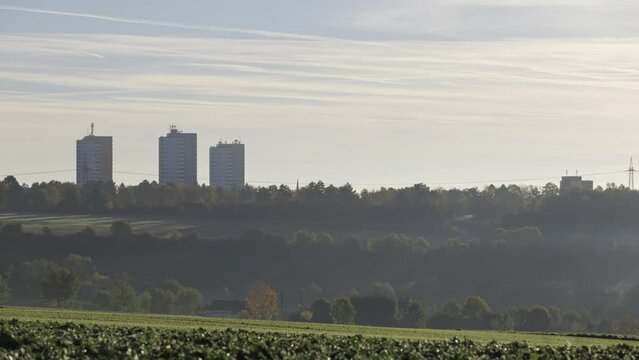 Time lapse shot of three high rise apartment buildings on top of fields and woods on a sunny morning in autumn with some mist
