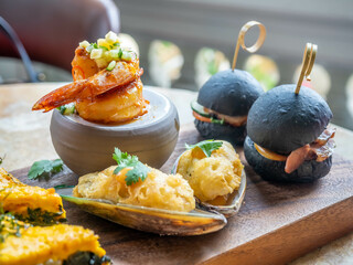 Variety of snacks in High tea set in luxury hotel in Bangkok, eg. charcoal mini burger, fusion shrimp recipe, little pizza.