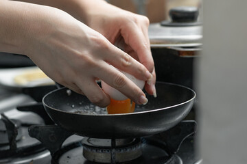 detailed shot of a girl's hands opening an egg and pouring it into the small frying pan to prepare...
