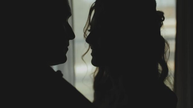 Silhouette of a man and woman in love kissing by the window, tenderness. Medium shot Silhouette of newlywed couple. Marriage, romantic atmosphere.