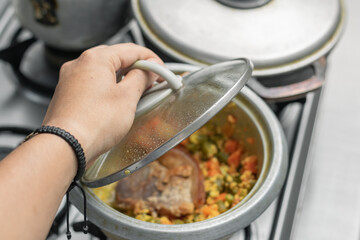 a girl's hand grasping the glass lid of a pot containing healthy food. pot on top of a gas stove.