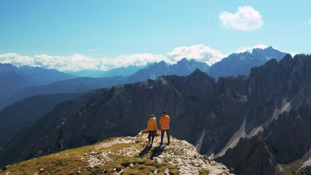 Couple of tourists stands over precipice in mountains. Young man and woman admire landscape of Three Peaks of Lavaredo fron hill edge aerial view