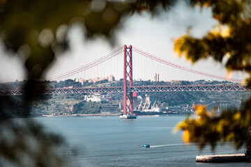The famous 25 April Bridge in Lisbon seen through the leaves of a tree
