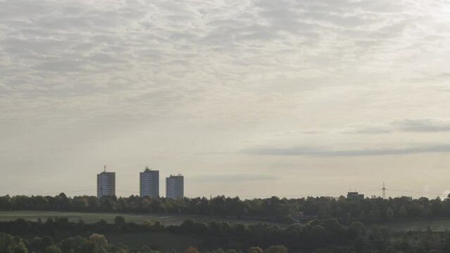 Time lapse shot of three high rise apartment buildings with colorful trees and the sun shining through the clouds on a morning in autumn