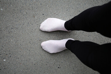 Woman standing on a grey concrete floor while wearing black leggings and pink socks. Color image of unrecognizable person. - Powered by Adobe