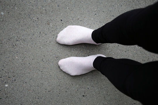 Woman standing on a grey concrete floor while wearing black leggings and pink socks. Color image of unrecognizable person.
