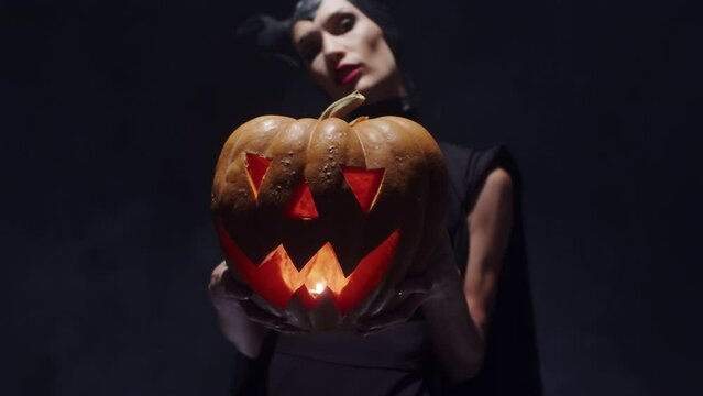 Fantasy woman witch with a pumpkin in her hands on Halloween on a black background, close-up, in a dark room