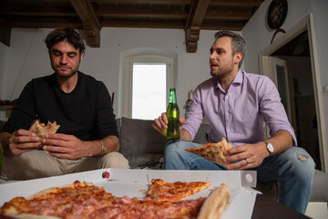 Two young men friends in their 30s spending time together enjoying pizza at home