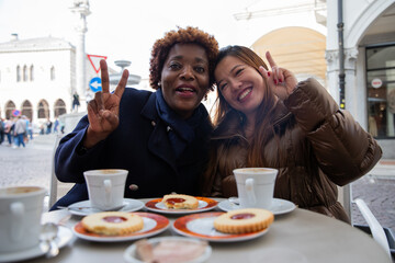 Two smiling multiracial friends enjoy their breakfast making a victory sign