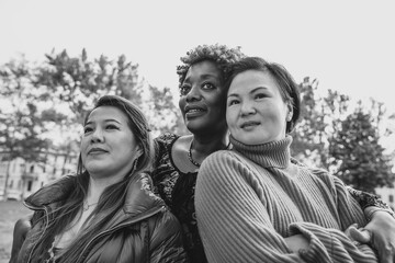 Black-and-white photo of three multiracial friends embracing at the city park looking up