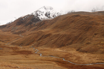 The river flows through an autumn valley. Snow-capped mountain peaks. The silence of nature