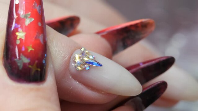 Applying a three-dimensional pattern with rhinestones and broths on the nail. The work of a manicure master. Nail design. A pattern of rhinestones on a prepared nail plate.