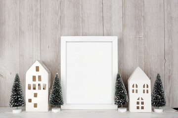 Christmas mock up with white frame, white houses and tree decor. Portrait frame on a wood shelf...