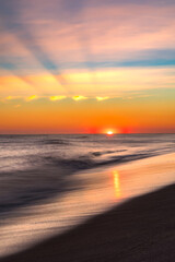 Vibrant sunset over the ocean as the sun dips below the horizon creating crepuscular rays and sunbeams . Long Island New York