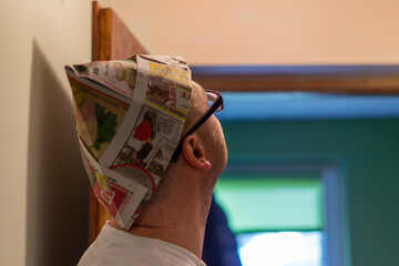 Mężczyzna patrzący w górę przygotowuje się do malowania pomieszczenia. Czapka z gazety chroniąca głowę przed farbą. - obrazy, fototapety, plakaty