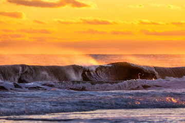 Spray from large waves in rough surf being lit up with golden light at sunset. Long Island New York