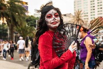 Mujer joven caracterizada como catrina con abanico negro y vestido rojo en el desfile de las...