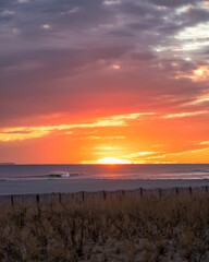 Fototapeta premium Calm beach scene under a vibrant sunset as the sun dips below the horizon. Long Beach, Long Island New York