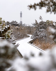 Snowy boardwalk path leading to a lighthouse in a wintery scene. Fire Island Long Island New York