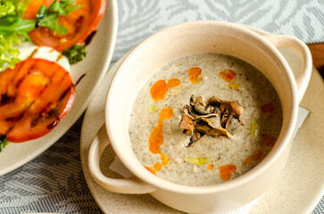 Bowl of mashed mushroom soup with truffle oil, in a restaurant, next to it is a tomato and mozzarella salad