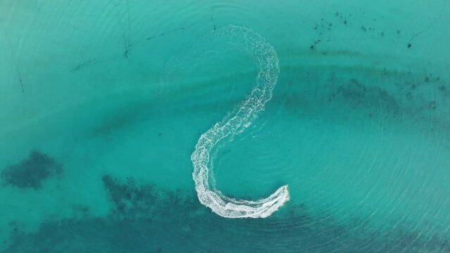 Tourist playing a jet ski or scooter above fast water scooter in the sea, going around in circle making beautiful white foamy waves in clear Pacific Ocean. clear turquoise at tropical beach. top view 
