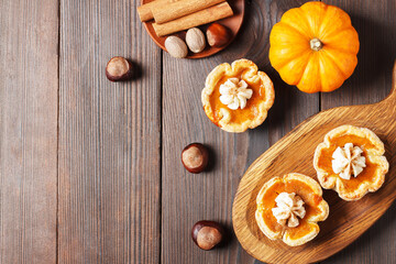 Pumpkin mini pies with whipped cream and spices on a wooden background. copy space