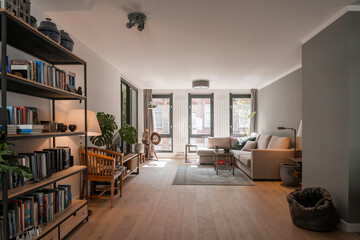 Living room interior in grey and brown colours, sofa, wooden floor, green plants and book shelves
