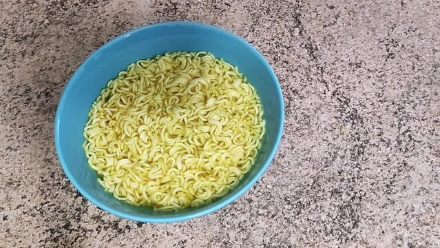 Timelapse instant noodles ramen in hot water, yellow pasta swelling and widening in blue bowl, poor people food at home