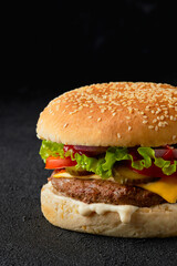 Close up classic traditional cheeseburger with beef, tomato, lettuce, pickles and onion on black background