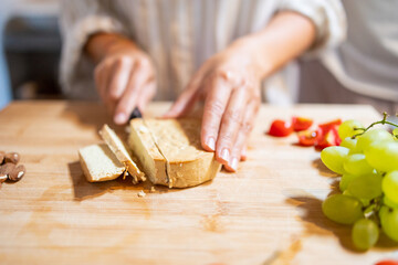Female hands cutting slices of almond vegan cheese for breakfast