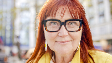 Portrait of middle aged red haired woman with glasses on looking to camera confidently