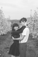 Young strong love between two young people walking under apple trees. Candid portrait of a couple in casual clothes. Affection of two people. Black and white portrait