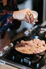 woman adding salt to organic chicken cooking  in a cast iron skillet