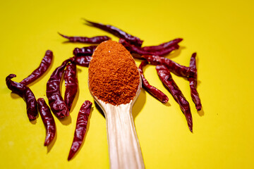 Spoonful of red chilli powder and dried red chillies on yellow background.