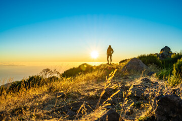 Siluette einer stehenden Frau, die die schöne Berglandschaft des Pico do Ariero bei Sonnenaufgang...