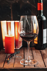 Red wine in glass. Glass of red wine are on the table. A candle, books and a bottle of wine on the table.