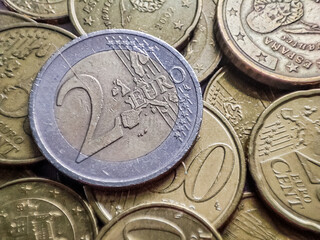Two euros coin close up detail with smaller euro coins around it on white background, savings in financial crisis