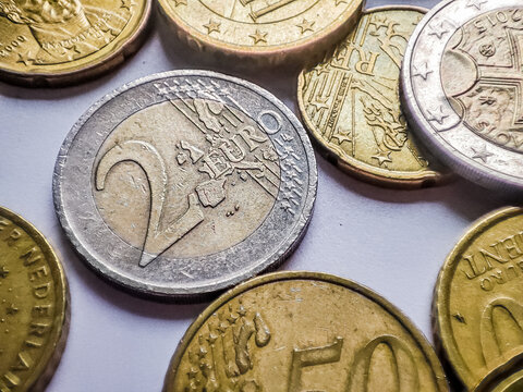 Two euros coin close up detail with smaller euro coins around it on white background, savings in financial crisis