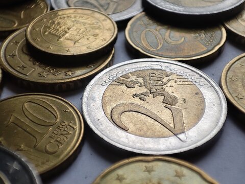 Two euros coin close up detail with smaller euro coins around it on white background, savings in financial crisis