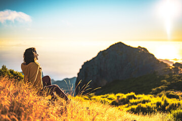 Woman sitting on a mountain meadow enjoying the beautiful mountain landscape of Pico do Ariero at...