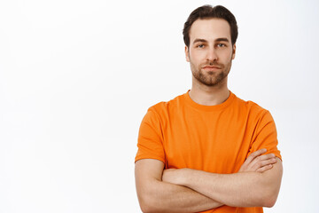 Handsome european man cross arms on chest, looking confident and self-assured, standing in orange...