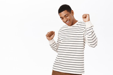 Dancing african american man having fun, smiling pleased, posing over white background in casual...