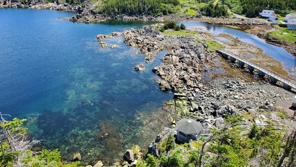 Aerial view of water in a lagoon with a bridge and a gazebo on a rocky coast, surrounded by trees