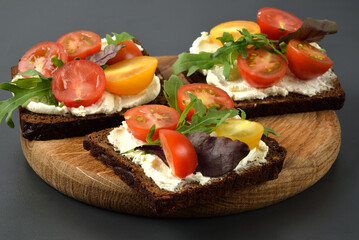 Bruschetta with tomato, arugula and soft cheese on wooden tray