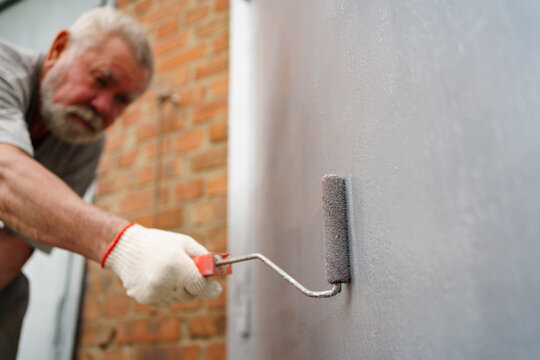 selective focus. an elderly man paints the metal garage door with a roller. 