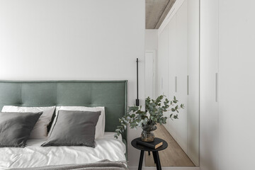 Modern minimalistic bedroom interior design in grey shades with light green bed, eucalyptus in glass vase, concrete ceiling. Scandinavian style.  Aesthetic simple interior design concept.